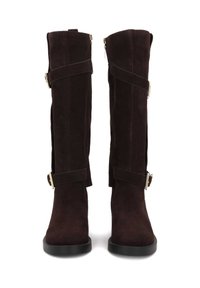 Knee-high brown suede boots with a square toe, fitted shape, side zippers, and decorative straps with metallic buckles. Flat soles.