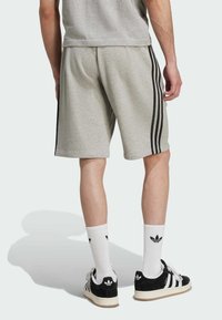Grijze katoenen shorts met drie zwarte zijstrepen, gecombineerd met zwart-witte sneakers en witte sokken met een zwart logo.