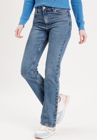 Fitted blue denim jeans with a high waist, featuring five pockets, light fading, and subtle stitching. Paired with multicolored sporty sneakers.