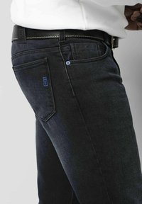 Dunkelblaue Jeans mit schmalem Schnitt, versehen mit einem blauen Logo-Patch auf der Gesäßtasche, kontrastierenden Nähten und einem schwarzen Ledergürtel.