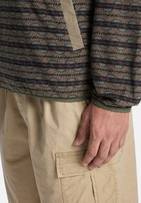 Φλις με καφέ, μπλε και πράσινο μοτίβο, με αντίθετη μπεζ πάνελ και μανσέτες, συνδυασμένο με μπεζ παντελόνι cargo.