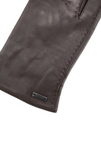 Braune Lederhandschuh mit einer strukturierten Oberfläche, Kontrastnähten und einem kleinen metallischen Logo-Detail nahe dem Saum. Glatte Oberfläche, taillierte Passform.