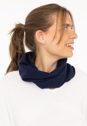 Navy blue infinity scarf made of soft, textured fabric, worn loosely around the neck, paired with a white sweater featuring a v-neck design.