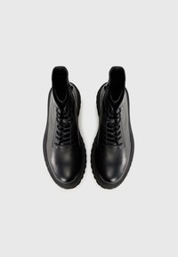 Stivali alla caviglia in pelle nera con lacci, dalla finitura liscia, punta rotonda e suola in gomma spessa. Presentano cuciture rinforzate e un design minimale.