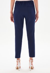 Pantaloni blu navy con una cintura elastica, gambe affusolate e una tasca sul retro. Completati da sandali alti bianchi.