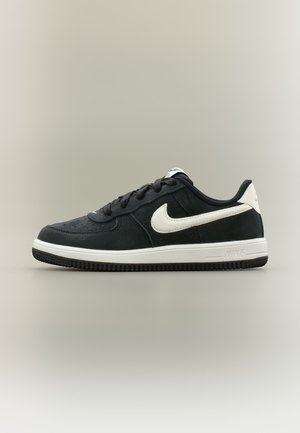 Baskets basses noires avec le swoosh Nike blanc et une semelle blanche, lacets noirs et semelle extérieure texturée, vues de profil sur un fond uni.