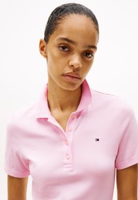 Rožu polo krekls ar īsām piedurknēm, ar apkakli un nelielu zīmola logo kreisajā krūtīs. Tekstūrēta auduma izpilde ar pogām.