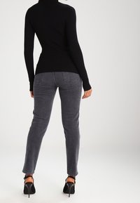 Black ribbed turtleneck sweater paired with gray skinny jeans, featuring back pockets and high-heeled shoes with ankle straps.