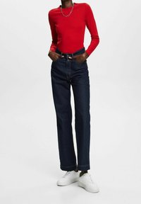 Red long-sleeve top with scalloped neckline, high-waisted dark blue denim jeans, and white sneakers. Casual fit with visible stitching details.