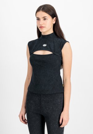 Naine pikkade tumedate juustega, kes kannab varrukateta musta tippi kõrge kaelusega ja lõikega detailiga rinna kohal.