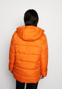 Chaqueta acolchada de color naranja brillante con capucha, que presenta costuras horizontales y una textura suave, que llega hasta la mitad del muslo.