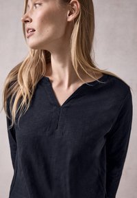 Marineblaues Langarmhemd mit V-Ausschnitt und Knopfdetails. Der Stoff hat eine weiche Textur, weist eine lockere Passform auf und zeigt dezente Nähte.