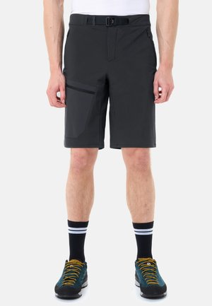 Mann trägt schwarze knielange Shorts mit Seitentasche, schwarze Socken mit weißen Streifen und türkisfarbene Wanderschuhe mit gelben Schnürsenkeln.