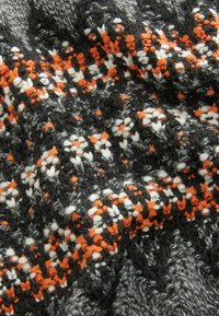 Gebreide stof met een textuurpatroon in grijs, zwart en oranje, met contrasterende witte accenten. Zacht en warm, met een indrukwekkend vakmanschap.