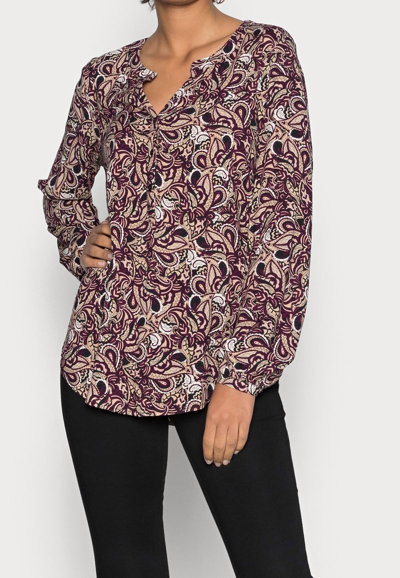 Blusa a maniche lunghe di colore bordeaux con motivo paisley, dotata di scollatura a V e dettaglio con bottoni al colletto. Realizzata in tessuto leggero.