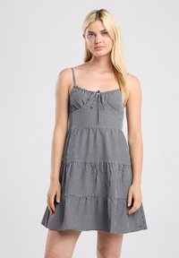 Black and white gingham dress with adjustable spaghetti straps, ruffled tiers, and a center bow detail. Cotton blend fabric.