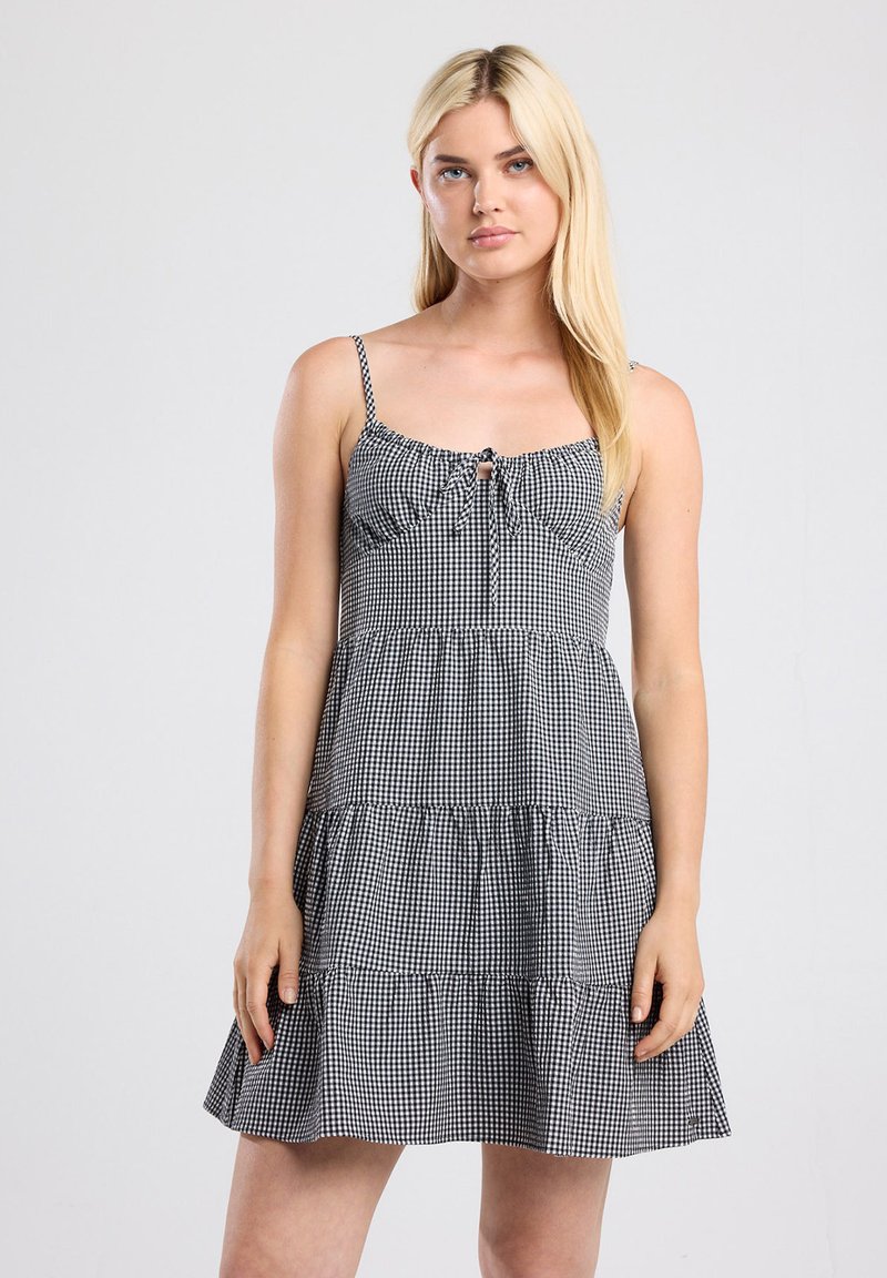 Black and white gingham dress with adjustable spaghetti straps, ruffled tiers, and a center bow detail. Cotton blend fabric.