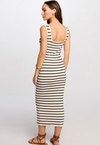 Robe midi rayée en beige et noir, avec un dos dégagé, une silhouette ajustée et de larges bretelles. Portée avec des sandales brunes à lanières.