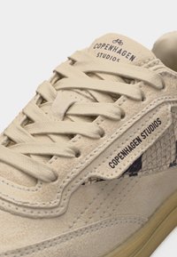 Baskets en daim beige avec lacets assortis, panneau latéral à texture croco et marquage "Copenhagen Studios" sur la languette et le côté.
