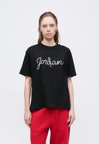 Maglietta nera in cotone con la scritta "Jordan" in strass e un piccolo logo. Fit rilassato con maniche corte e scollatura rotonda.
