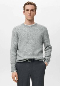 Maglione grigio lavorato a maglia con motivo a spina di pesce, scollo arrotondato e polsini a costine, abbinato a pantaloni scuri. Tessuto morbido e vestibilità comoda.