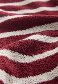 Tessuto a righe bordeaux e crema con un motivo intrecciato e strutturato. Le onde creano una superficie morbida e tattile che aggiunge profondità.