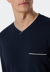 Marineblauw V-hals shirt gemaakt van zachte stof, met een borstzak met een witte gestreepte accent en een contrasterende witte halslijn.