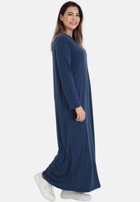 Long navy blue dress in soft fabric with long sleeves, a round neckline, and a flowy design, paired with white sneakers.
