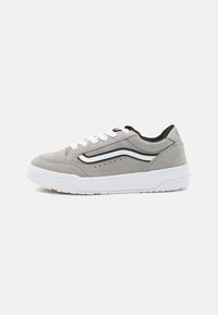 Grijze suède sneaker met witte veters, zwarte accenten en een textuur witte zool. Heeft een zijstrip en perforaties op het bovenwerk.