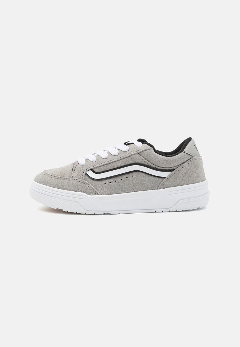 Grijze suède sneaker met witte veters, zwarte accenten en een textuur witte zool. Heeft een zijstrip en perforaties op het bovenwerk.