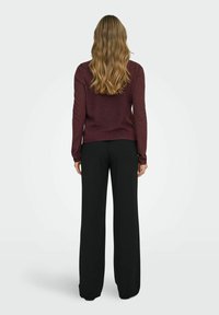 Jersey burdeos de manga larga combinado con pantalones negros holgados, mostrando una textura suave y un ajuste relajado desde una vista trasera.