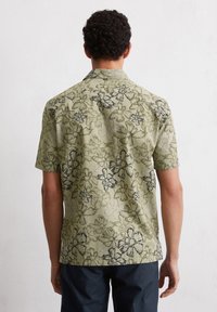 Korte mouwen shirt van olijfgroene stof met een donker bloempatroon. Heeft een camp collar en een relaxte pasvorm met zijnaad.