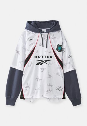 Valge kapuutsiga dressipluus, millel on segu autogrammidest, mustadest ja punastest detailidest ning tumehall kapuuts. Valmistatud kergetest kangast, spordi disainiga.