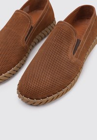 Chaussures slip-on en suède marron avec un design perforé, des panneaux élastiques latéraux et une semelle en caoutchouc contrastée avec un accent cousu.