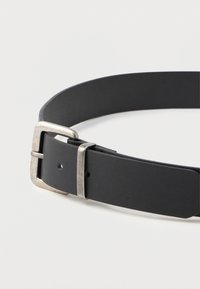 Zwarte leren riem met een zilveren rechthoekige metalen gesp en twee gaatjes, geplaatst op een witte ondergrond.