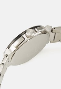 Montre en acier inoxydable avec un boîtier rond, finition métallique, couronne texturée et bracelet à maillons ; le dos est lisse et sans marque.