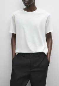 Hvid kortærmet t-shirt lavet af blødt stof, parret med sorte skræddersyede bukser, der viser et rent og minimalistisk design.