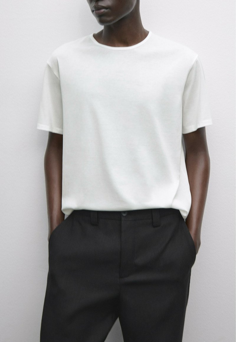 Hvid kortærmet t-shirt lavet af blødt stof, parret med sorte skræddersyede bukser, der viser et rent og minimalistisk design.