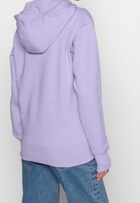 Felpa viola chiaro con cappuccio ampio, polsini e orlo ribattuti. Realizzata in tessuto morbido, presenta una vestibilità rilassata e una texture liscia.