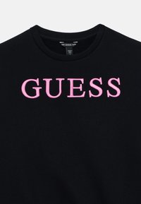 Μαύρο φούτερ με στρογγυλή λαιμόκοψη και ροζ κεντητό λογότυπο "GUESS" στο μπροστινό μέρος. Μαλακό ύφασμα με ομαλή υφή.