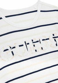 Valge T-särk, millel on mereväe sinised horisontaalsed triibud; "GUESS" logo pehme valge ja heleda roosa sädelevate detailidega. Ümar kaelus, pehme puuvillane materjal.