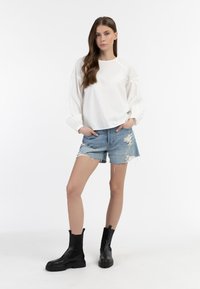 Weißes Langarmhemd, Denim-Shorts mit ausgefransten Säumen und schwarze Knöchelstiefel mit dicken Sohlen. Einfaches, lässiges Outfit mit kontrastierenden Farben.