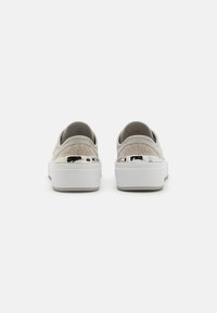 Lys beige sneakers med teksturert strikkoverdel, hvit såle og metalliske hælinnsatser, med rund tå og slip-on stil.