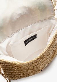 Borsa a tracolla intrecciata in paglia con esterno beige, interno in raso liscio di colore chiaro e una piccola tasca interna con l'etichetta "even&odd".