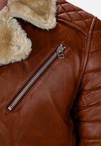 Giacca in pelle marrone con finitura texturizzata, design trapuntato sulle maniche e colletto in pelliccia sintetica con tasca frontale con zip.