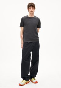 T-shirt noir à manches courtes associé à un jean noir ample et des baskets jaunes vives avec des accents orange, le tout sur un fond blanc.