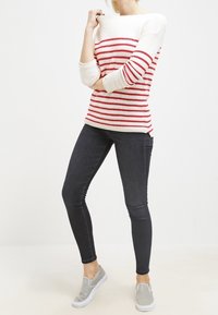Rot-weiß gestreifter Strickpullover mit schulterfreier Gestaltung, kombiniert mit eng anliegenden schwarzen Jeans und grauen Slip-On-Schuhen.
