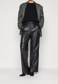 Pantalones de cuero negros con cintura alta y diseño de pierna recta, combinados con un suéter de punto negro texturizado y una chaqueta gris.