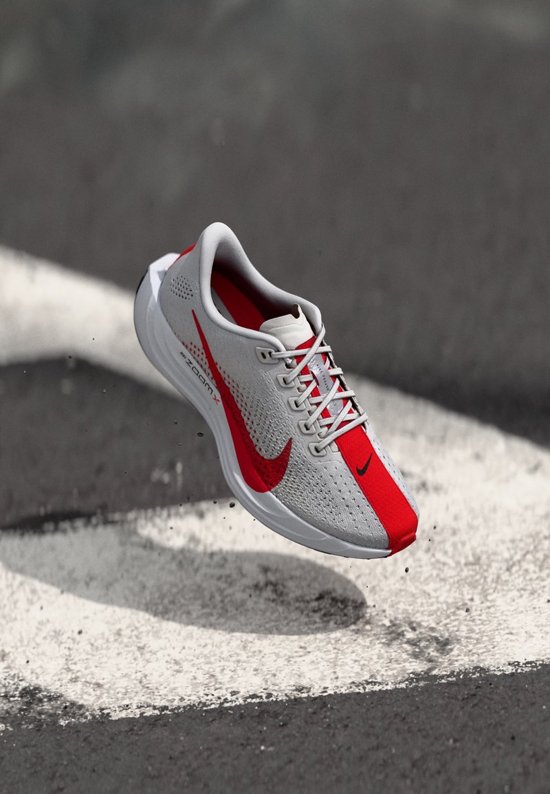 Lightweight running shoe with a grey mesh upper, red accents, and white sole. Features perforations and flat laces for a secure fit.