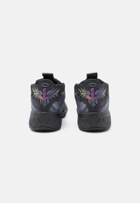 Baskets noires avec une surface texturée, présentant des motifs de logo colorés avec des ailes sur le talon et des tirettes pour un enfilage facile.